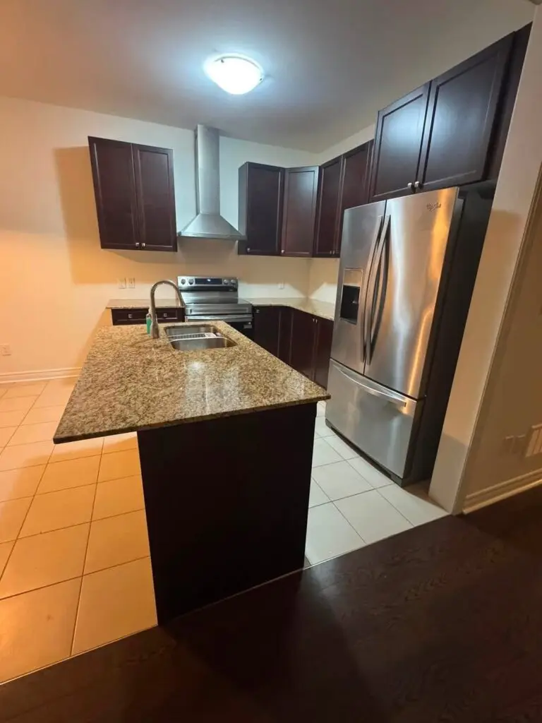 Clean kitchen with a granite island, dark cabinets and stainless steel appliances