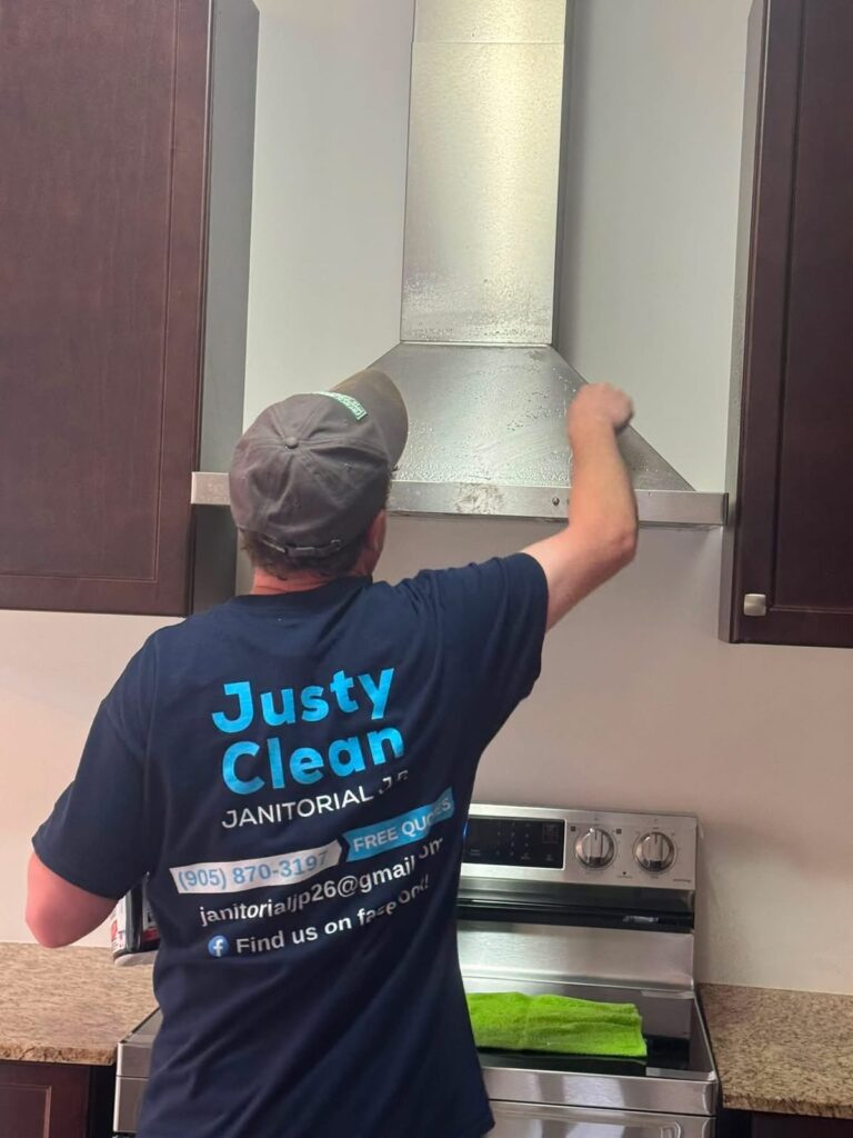 A JustyClean team member in a branded shirt cleaning a stainless steel range hood